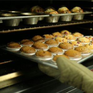 a person pulling muffin tins of muffins out of an oven